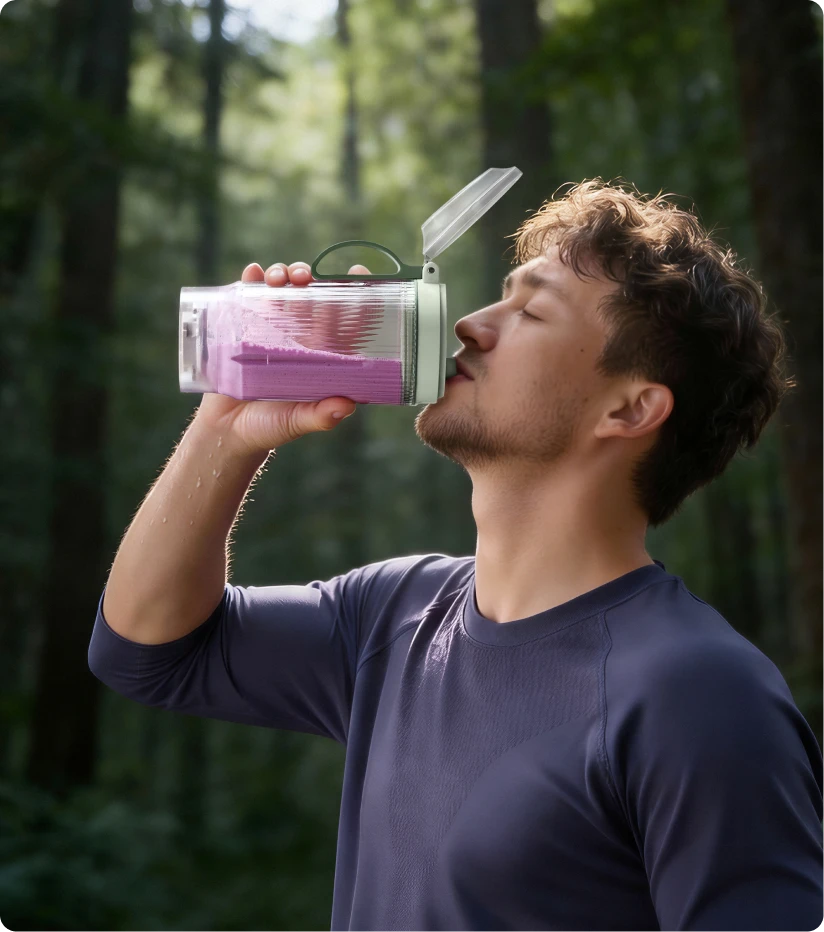 Utente che beve uno smoothie dal bicchiere portatile Dreame Portable Blender durante un'escursione nel bosco
