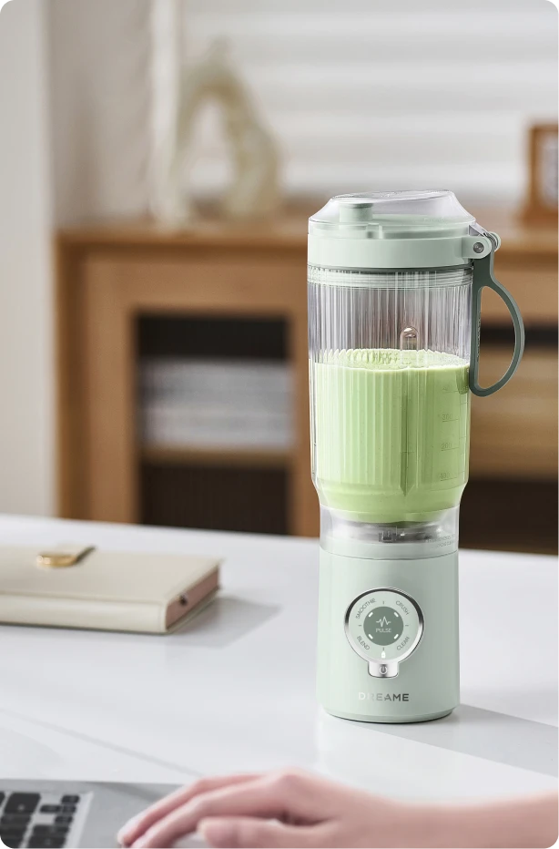 Dreame Portable Blender design senza fili su una scrivania in ufficio che mescola una bevanda verde durante il lavoro