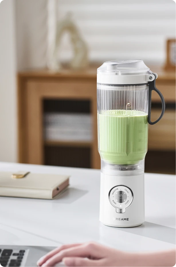 Dreame Portable Blender design senza fili su una scrivania in ufficio che mescola una bevanda verde durante il lavoro