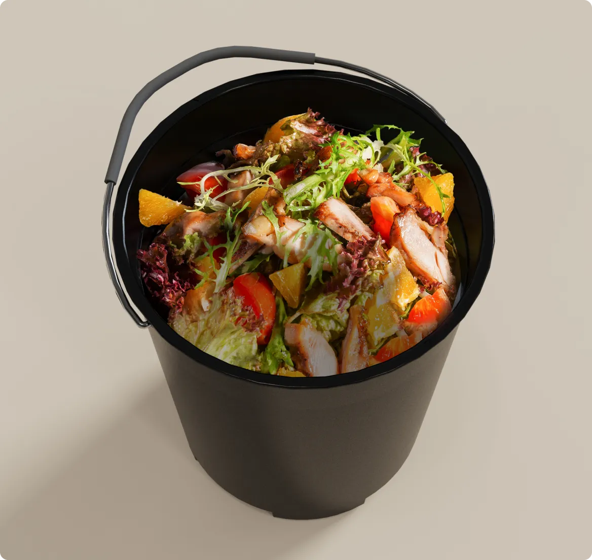 Un secchio nero da cucina pieno di scarti alimentari misti tra cui insalata, carne e verdure rappresenta i tipici rifiuti domestici quotidiani.